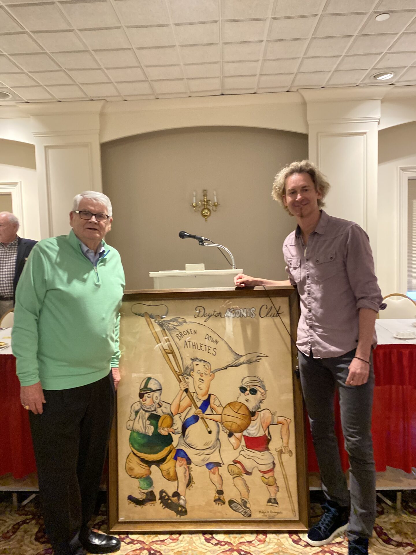 Two men standing next to a painting of three cartoon characters.